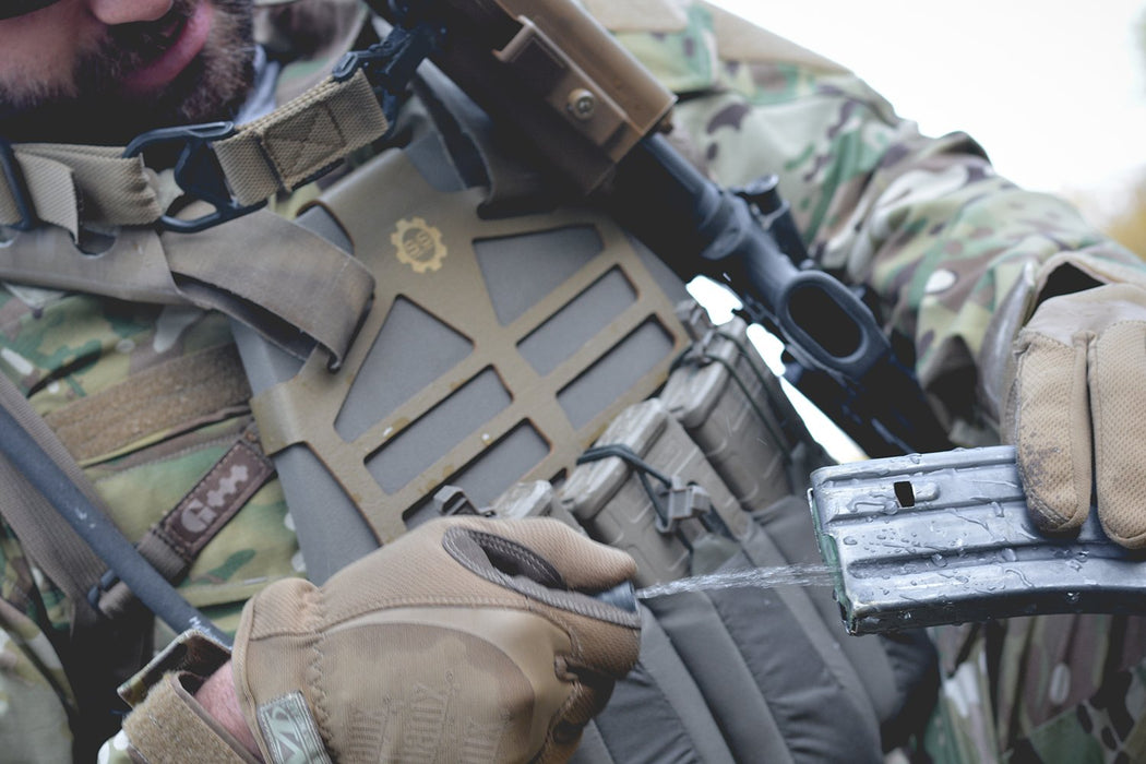 A solider using the Geigerrig Pressurized Hydration pack to clean off the ammo clip of his rifle.