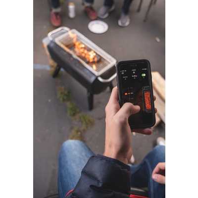Person using the BIolite FirePit app to manage the flame height output. People sitting around in chairs on pavement observing.