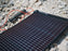 A lightsaver foldout solar panel charging a phone on a bed of rocks.