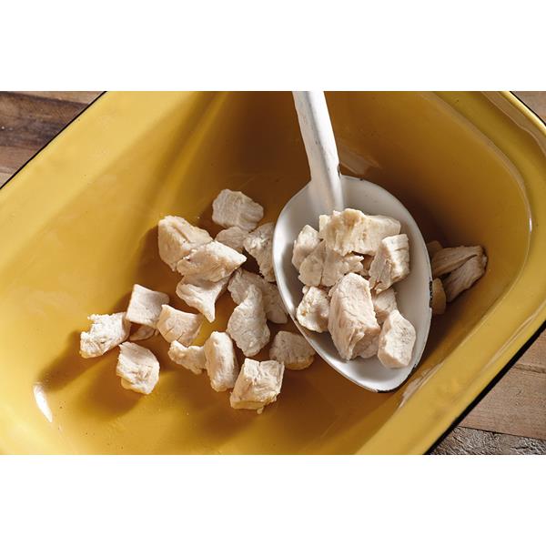 A white camping spoon scooping out freeze dried chicken bits from a mustard coloured bowl. In the background is a dark hardwood floor.