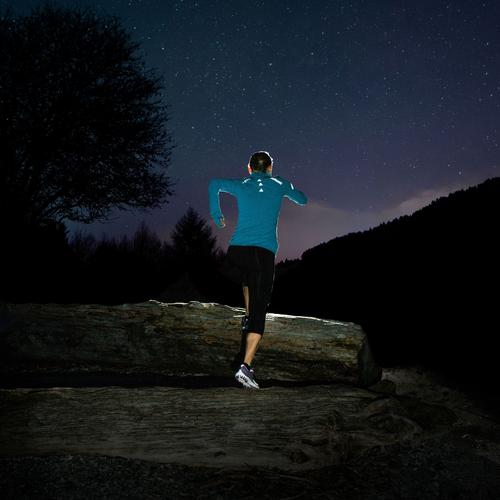 Woman jogging at night with a strips of Gear Aid's Tenacious Reflective Tape on her back.
