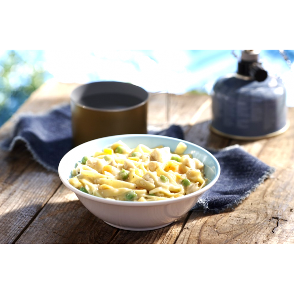 A white and blue coloured bowl of Happy Yak prepared chicken blanquette and egg noodles is set on a picnic table with a camping mug and hot kettle beside it.