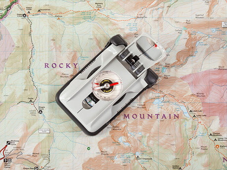 The Brunton TruArc 20 is placed on a map with the protective cover open showing the compass dial and degree indicator. The label 'Rocky Mountain' in large purple text shows on the map beneath the compass.