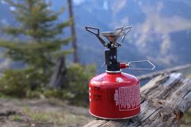 A MSR PocketRocket Mini camp stove sitting on a fallen tree on a hillside facing mountains. The camp stove propane tank is a bright red and the stove is black with the gas flow valve sticking out to the right.