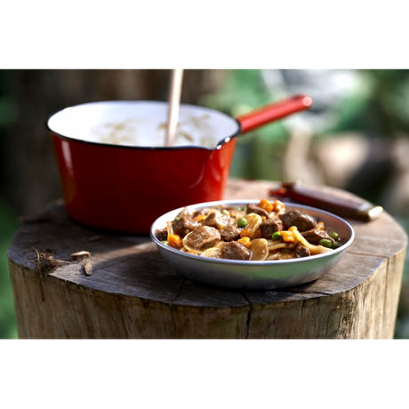 A bowl of beef stew from a Happy Yak freeze dried packet, beside a red camping pot on a tree stump.