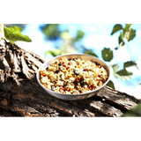 A silver stainless steel camping bowl full of the Happy Yak mediterranean Pork dish on a large tree branch wth green leaves surrounding it.