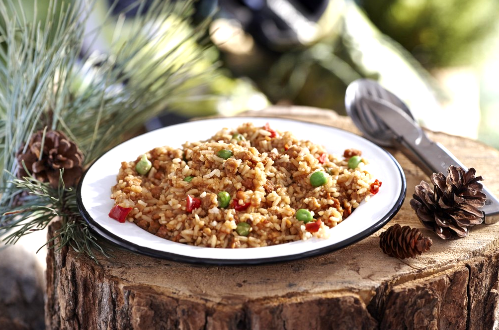 Happy Yak Express Teriyaki Rice (Soy, Peas, Sesame Seeds, Teriyaki sauce, and Red Bell Pepper). A plate of the Teriyaki Rice is shown laying on a tree stump beside a pine cone and camping utensils..