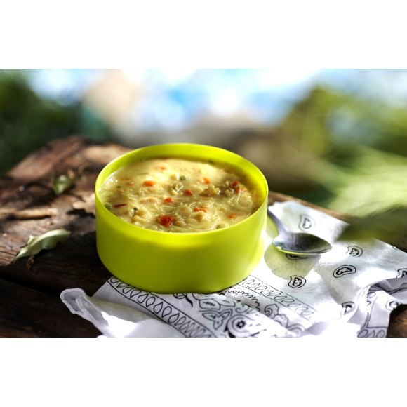 A lime green bowl of the boiled and mixed freeze dried Happy Yak Coconut Thai Soup with a napkin and camping spoon on top of a tree log.