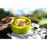 A lime green bowl of the boiled and mixed freeze dried Happy Yak Coconut Thai Soup with a napkin and camping spoon on top of a tree log.